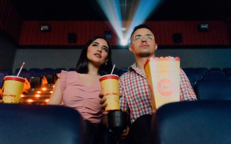 Kobieta i mężczyzna w okularach korekcyjnych oglądają film w kinie z popcornem i napojami w rękach